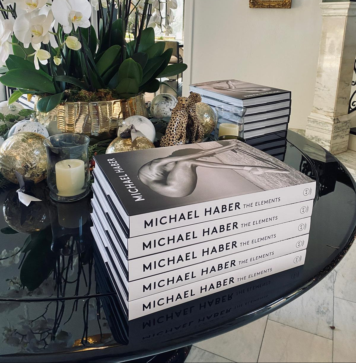 Stack of books titled 'The Elements' by Michael Haber on a table with decorative items including flowers and candles.